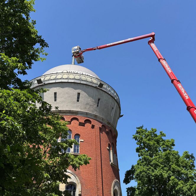 Blick vom Boden auf die Spitze des Turms, in dem sich die Camera Obscura befindet; ein Hubwagen mit ausgefahrener Plattform steht neben dem Turm.