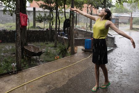 Frau in sommerlicher Kleidung tanzt glücklich auf einer Straße durch den Regen.