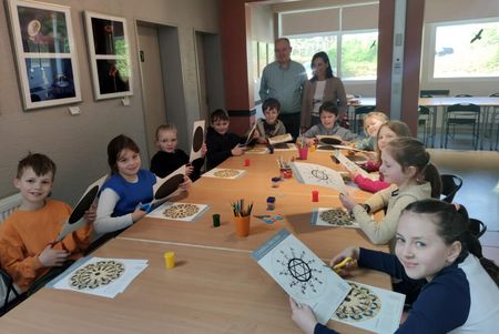 Schulkinder basteln im Workshopbereich der Camera Obscura ein Phenakistiskop (Lebensrad). Zwei Erwachsene stehen im Hintergrund. Alle Anwesenden lächeln in die Kamera.
